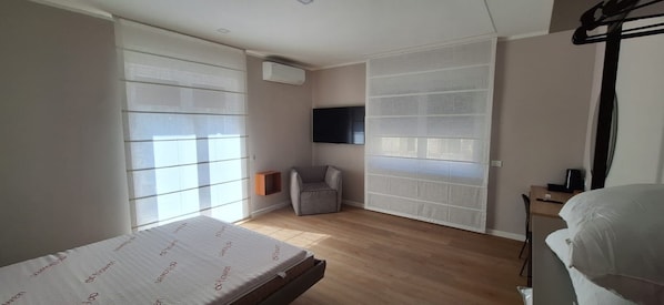 A bedroom with a bed, a chair, a TV, and a window with blinds.