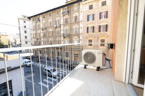 A balcony with a Samsung air conditioning unit, a view of a street with cars and a pedestrian crossing, and a building with multiple windows and balconies. - Lyda Bed&Room (La Spezia)