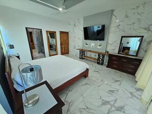 Ein Hotelzimmer mit einem großen Bett, einem Fernseher, einer Holzbank, einem Spiegel und Marmorböden.