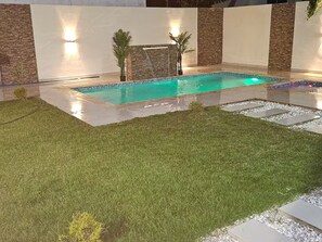 Ein Schwimmbecken mit Fliesenbordur, umgeben von einem gepflegten Rasen und einem Steinweg.