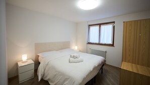 Una camera da letto con un letto, comodini, una finestra con tende, un termosifone e un armadio.