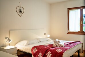 A neatly made bed with a red quilt, a bedside lamp, and a heart-shaped decoration on the wall.