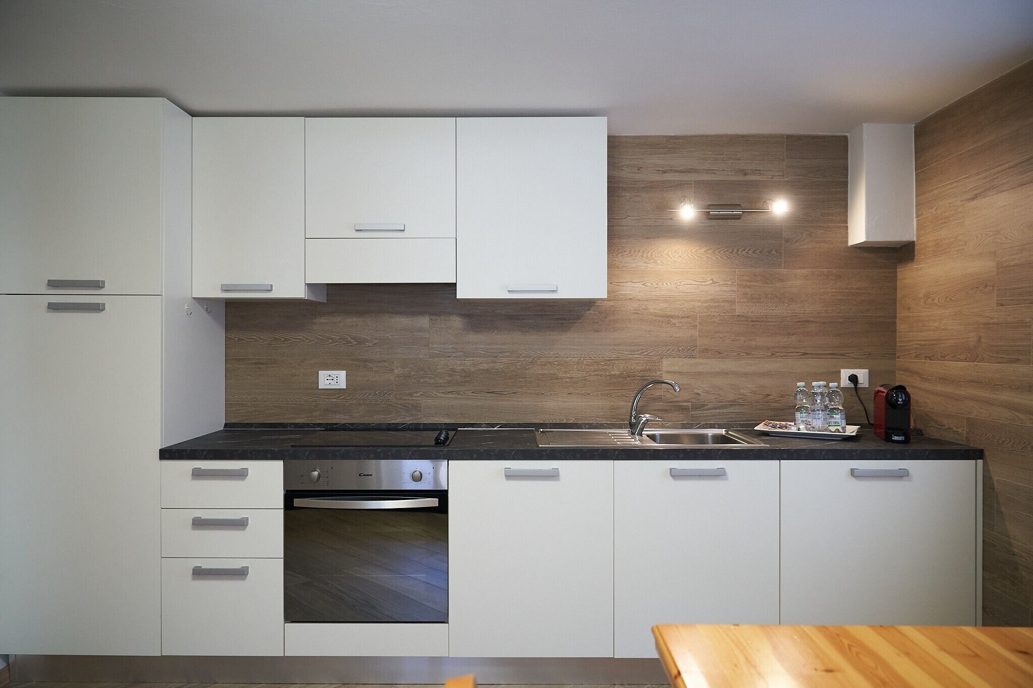 Eine moderne Küche mit weißen Schränken, einem Einbauofen, einer Spüle aus Edelstahl und einer Holz-Spritzschutzwand.