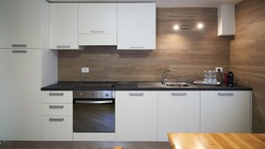 Una cucina moderna con mobili bianchi, forno integrato, lavello in acciaio inossidabile e piano di lavoro in legno.