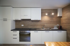 Eine moderne Küche mit weißen Schränken, einem Einbauofen, einer Spüle aus Edelstahl und einer Holz-Spritzschutzwand.