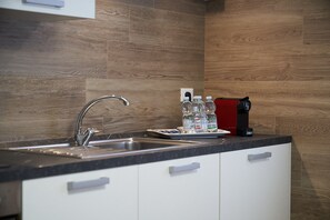 Eine Küche mit einem Edelstahl-Spülbecken, weißen Schränken und einer roten Kaffeemaschine.