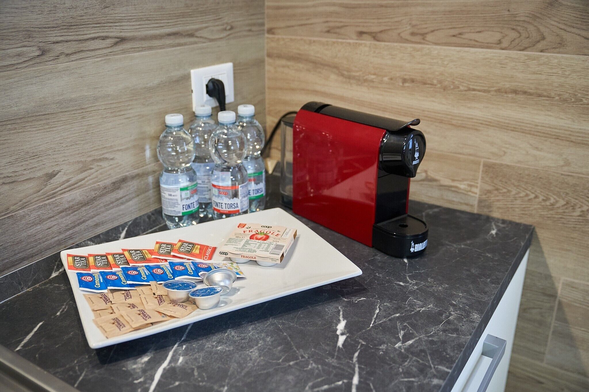 Een aanrecht met een koffieapparaat, waterflessen en theezakjes.