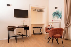 Ein Hotelzimmer mit Schreibtisch, zwei Stühlen, Fernseher, Kleiderhaken und Heizkörper.