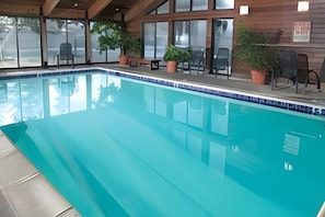 An indoor swimming pool with clear blue water, surrounded by potted plants and chairs. - CW BLOCK Steamboat 3br (Steamboat Springs)