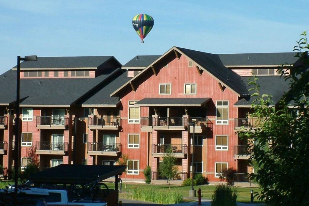 A multi-story building with balconies, a flat roof, and a hot air balloon in the sky.