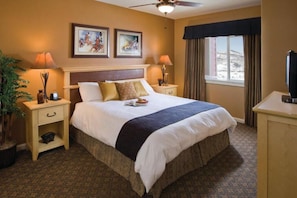A hotel room with a large bed, two bedside tables, a ceiling fan, a window with curtains, and artwork on the wall. - CW BLOCK Steamboat 3br (Steamboat Springs)