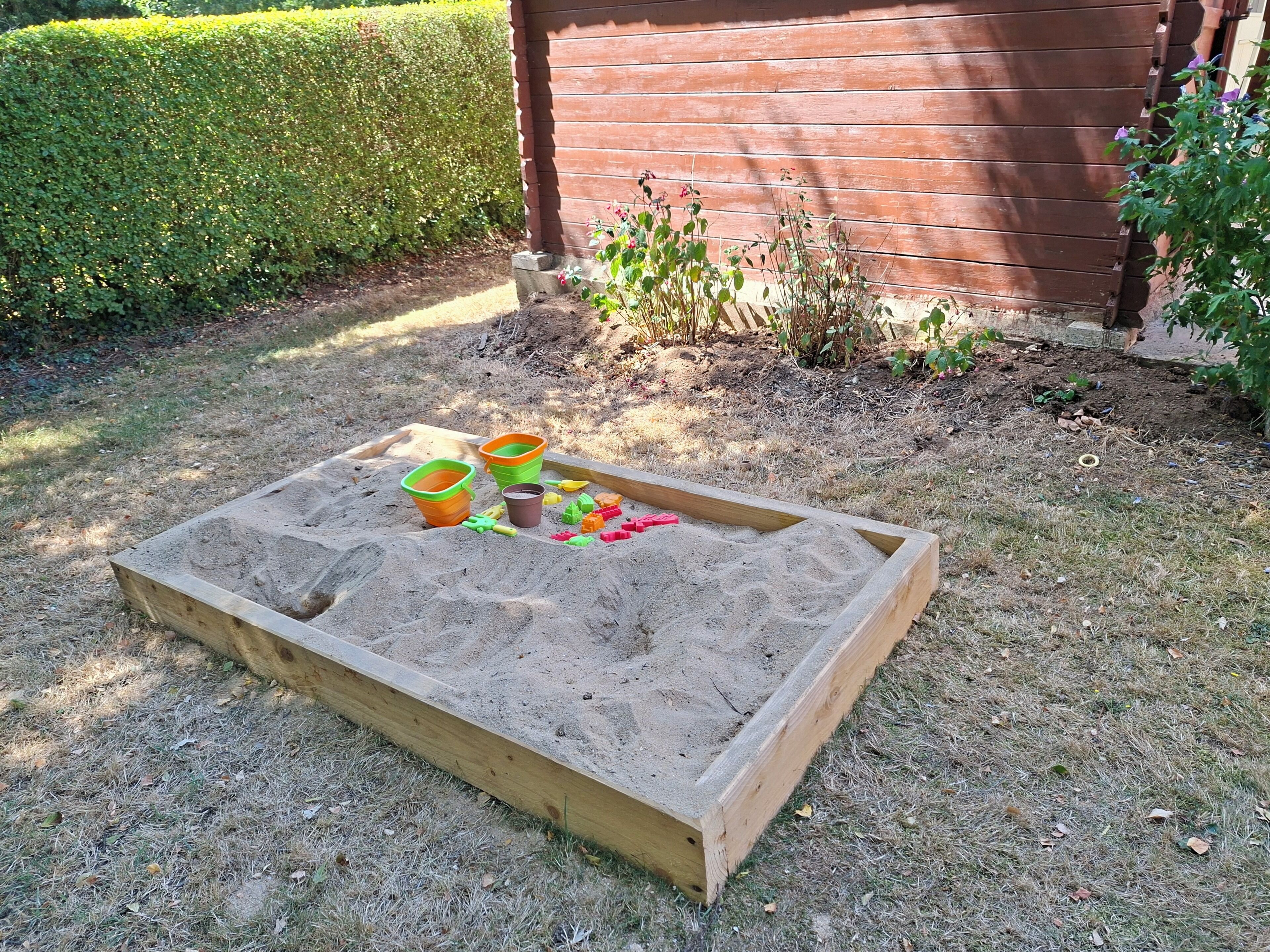 Ein Sandkasten mit Spielzeug und Eimern in einem Garten.