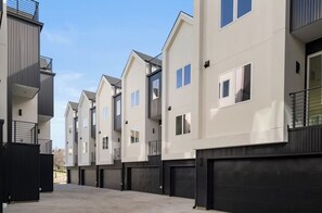 A row of modern multi-story residential buildings with balconies, large garage doors, and a clear sky. - Landing Amazing 3BD in Dallas (Dallas)