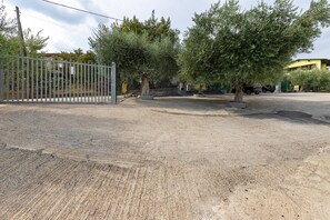 A gravel parking area with a metal gate, trees, and a building in the background.