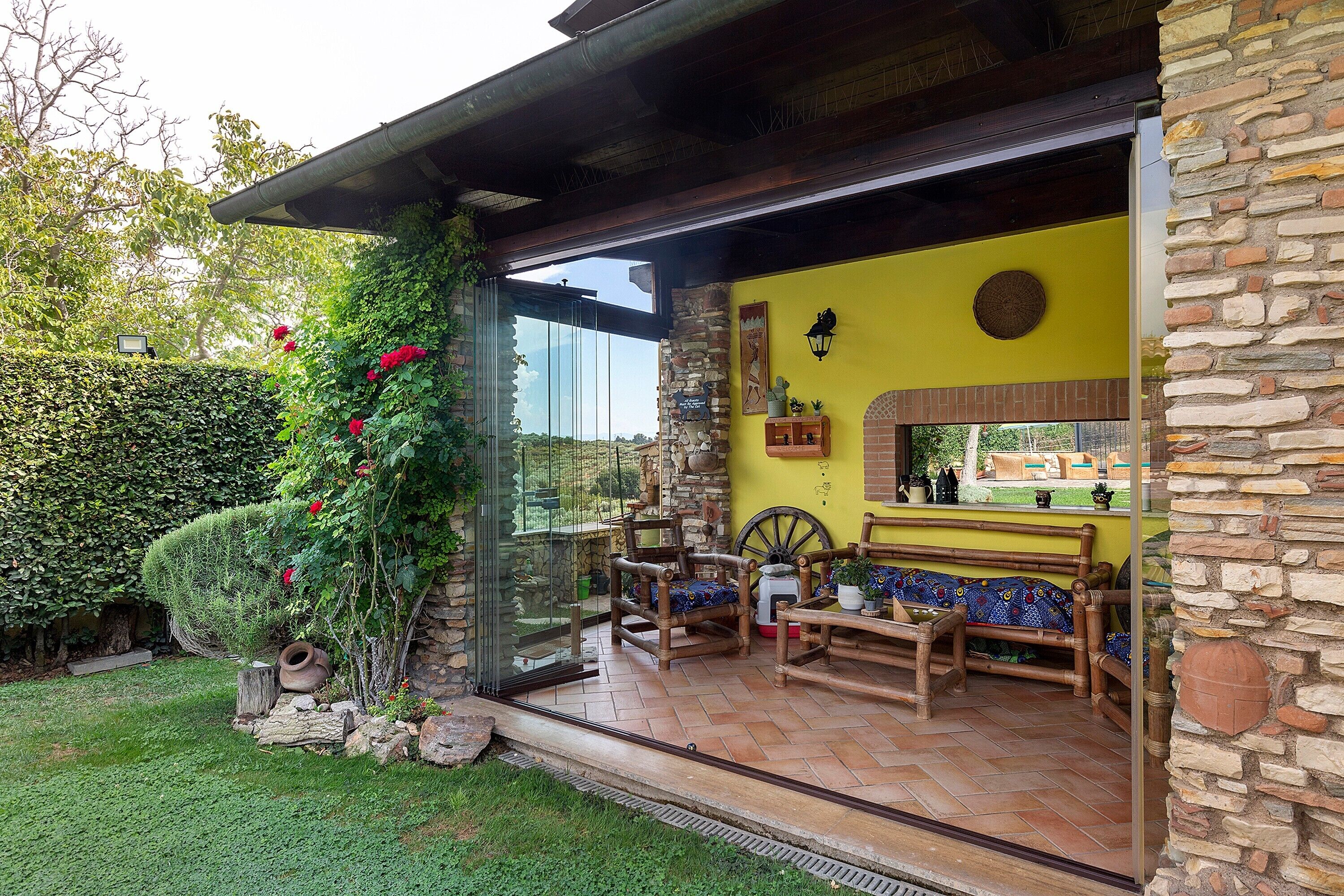 Une terrasse avec un mur en pierre, une porte vitrée donnant sur un jardin et du mobilier d’extérieur.