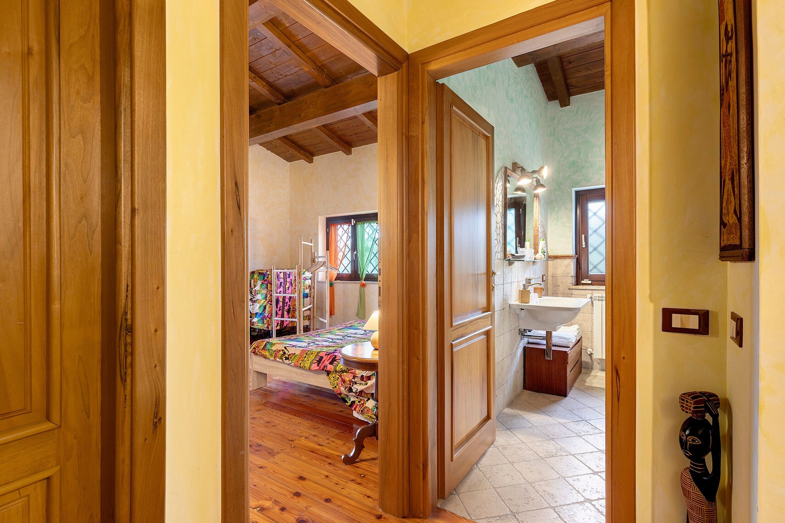 A room with a bed, a bathroom with a sink, and a wooden ceiling.