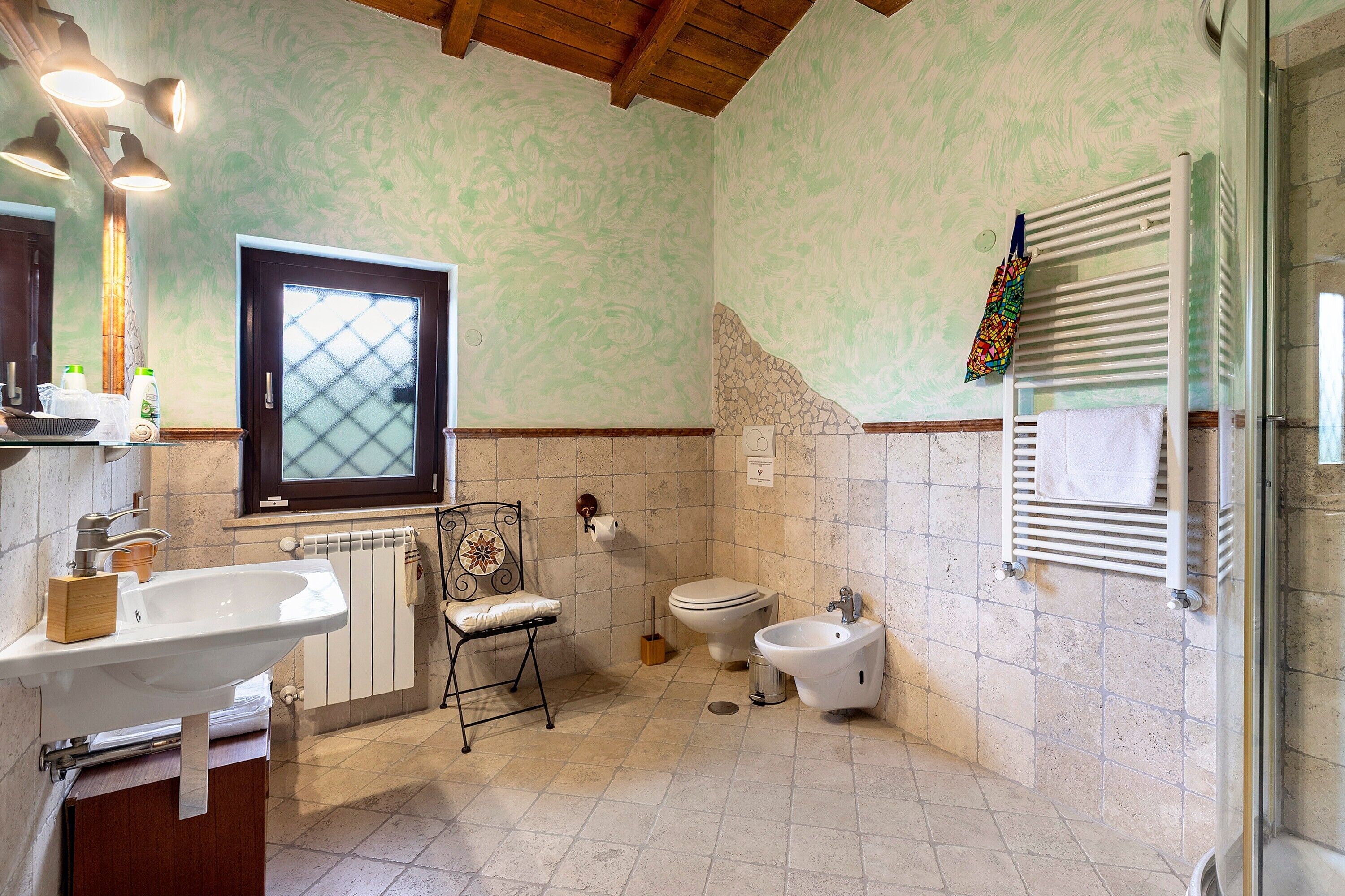 A bathroom with a sink, toilet, bidet, and a window with a frosted glass design.