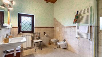 A bathroom with a sink, toilet, bidet, and a window with a frosted glass design.