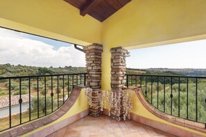 A balcony with a yellow wall, a stone pillar, and a view of a rural landscape.