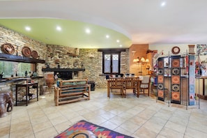 A cozy living room with a stone wall, a fireplace, a dining area with wooden furniture, and a colorful rug.