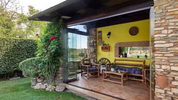 Une terrasse avec un mur en pierre, une porte vitrée donnant sur un jardin et du mobilier d’extérieur.