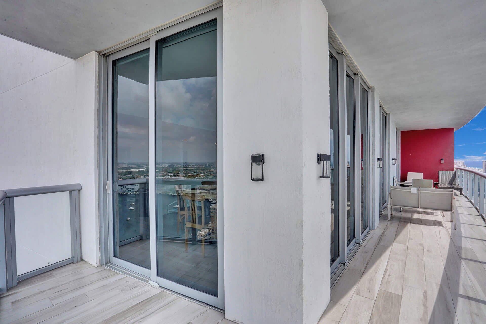 Ein Balkon mit Glastür, die zu einem Zimmer führt, einer roten Wand und Blick auf eine Stadtansicht.