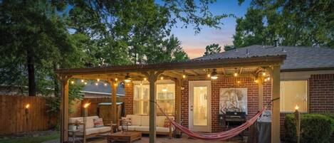 A covered patio area with a hammock, outdoor seating, and string lights.