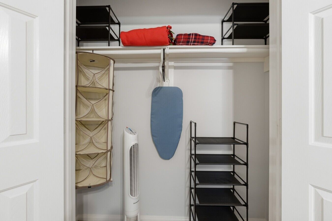 Un vestidor con estantes, un cubrearmarios para colgar, una funda para ropa azul y un calentador portátil blanco.