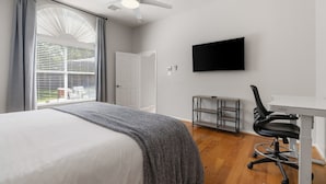 Un dormitorio con cama, escritorio, silla, televisor y ventilador de techo.