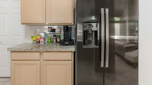 Una cocina con un refrigerador de acero inoxidable, una cafetera y diversos alimentos sobre la encimera.