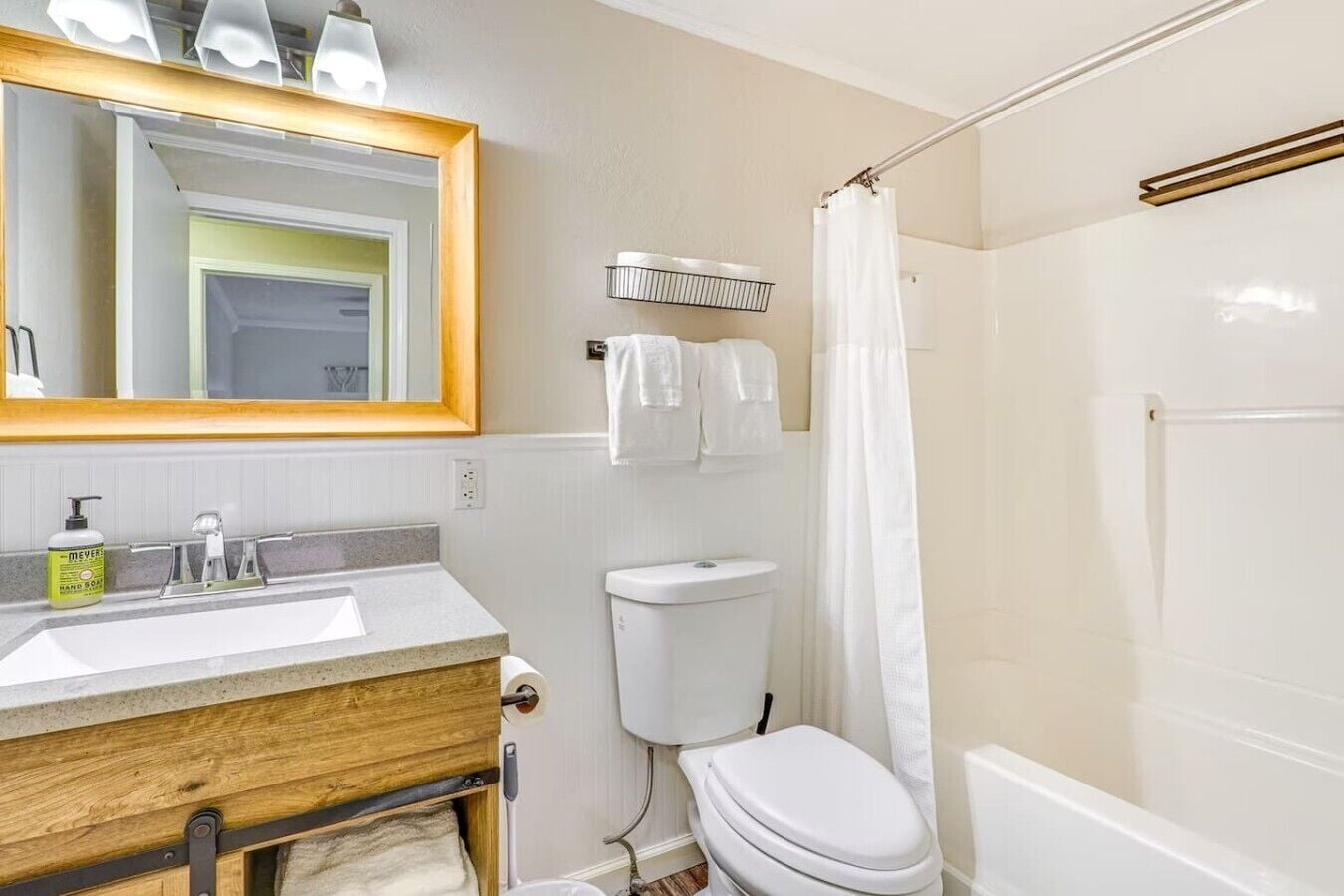 Une salle de bain avec un meuble-lavabo en bois, des toilettes blanches, une douche avec un rideau et un miroir avec éclairage intégré.