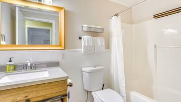 Une salle de bain avec un meuble-lavabo en bois, des toilettes blanches, une douche avec un rideau et un miroir avec éclairage intégré.