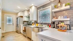 Una cocina moderna con armarios blancos, electrodomésticos de acero inoxidable y un amplio ventanal.