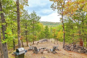 A forested campsite with a grill, chairs, and a fire pit. - Haysy Hollow House, Fire Pit, Backyard (Eureka Springs)