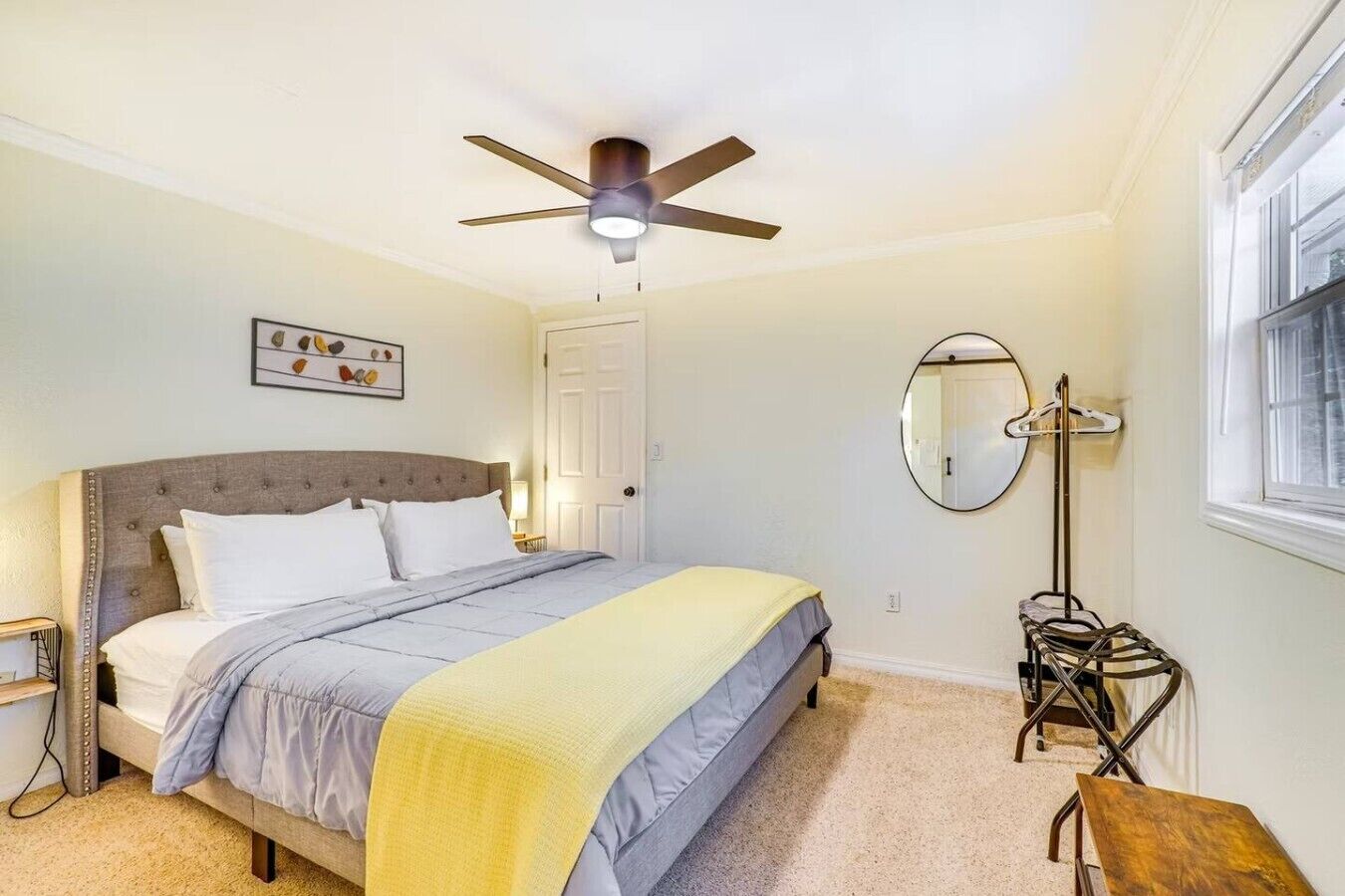 Ein Schlafzimmer mit Bett, Deckenventilator, Nachttisch, Spiegel und Fenster.