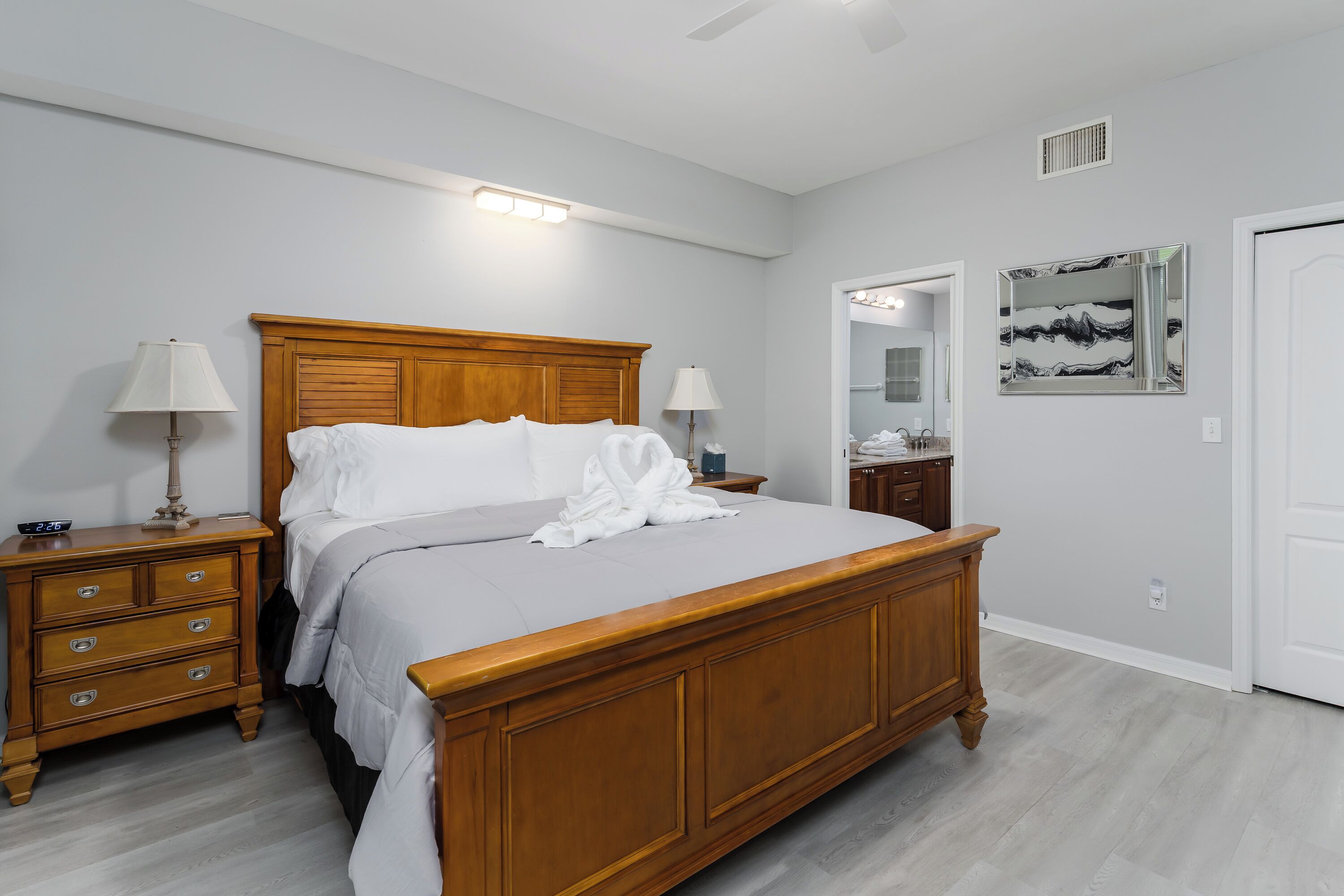 A bedroom with a wooden bed, bedside tables, a nightstand, a mirror, and a wall-mounted light fixture.