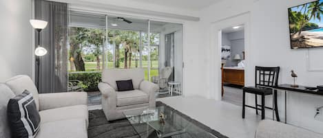 A modern living room with a glass coffee table, grey sofas, and a view of a garden through large windows.