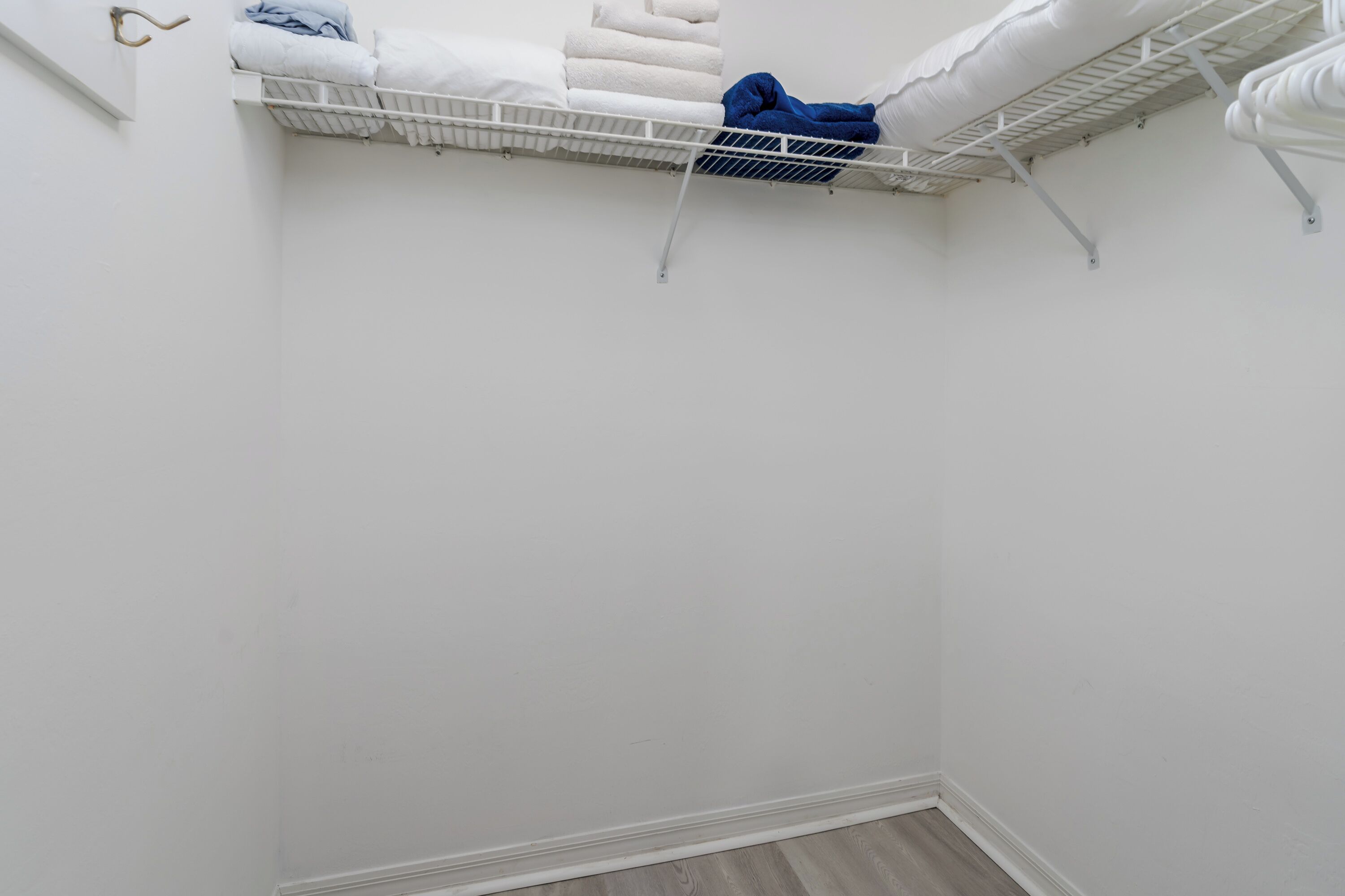 Esquina de una habitación con una pared blanca y un suelo blanco. Hay un estante blanco con toallas blancas y azules dobladas.