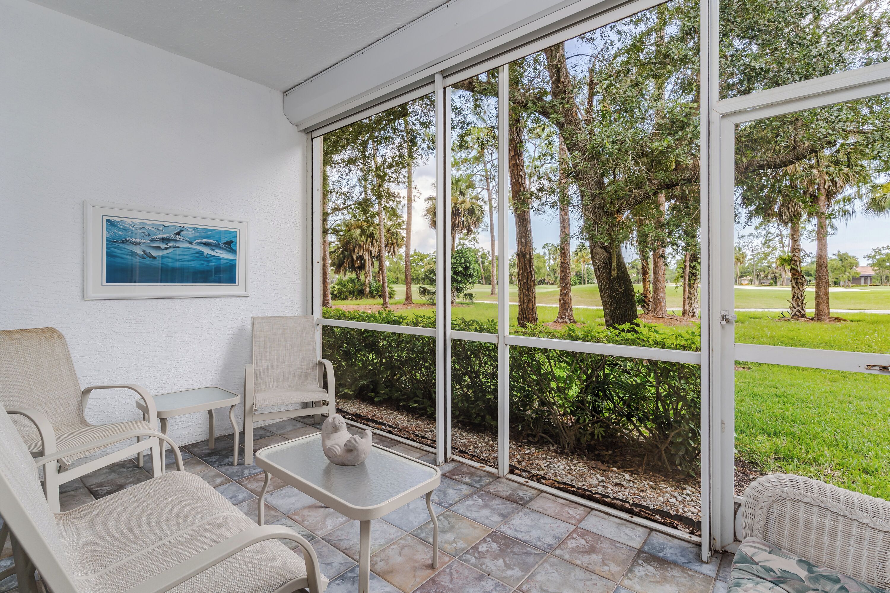 A room with a large window, a framed picture, and a seating area with chairs and a table.