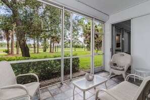 Ein Zimmer mit großem Fenster und Blick auf einen Golfplatz, möbliert mit weißen Korbstühlen und einem kleinen Tisch.