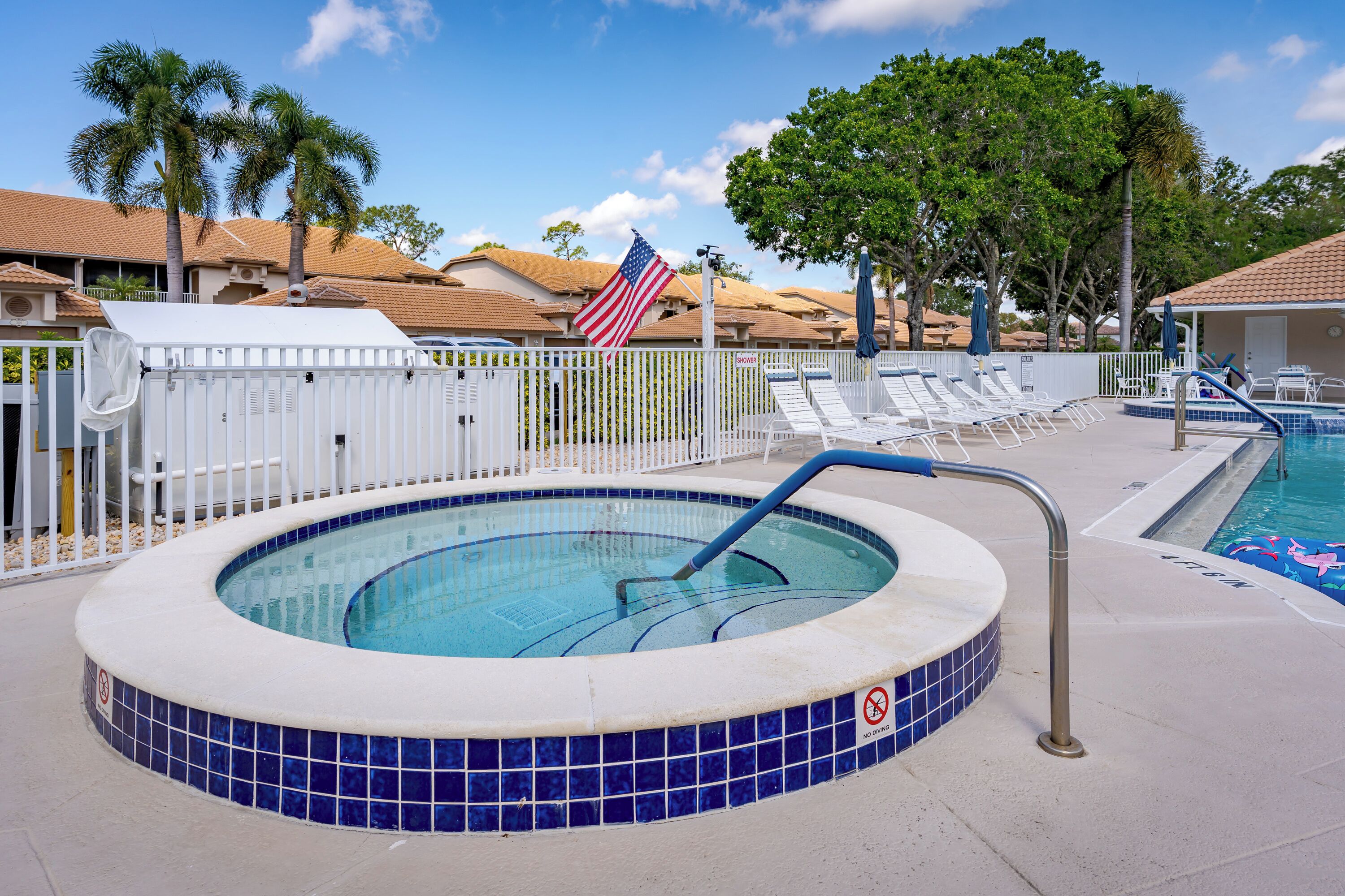 A swimming pool with a no diving sign, a flag, and lounge chairs.