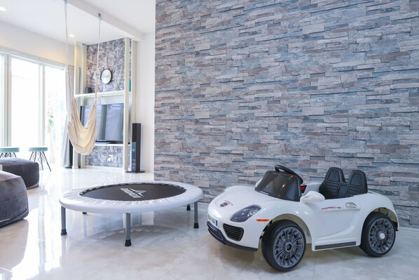 A modern living room with a stone wall, a white convertible toy car, and a trampoline.