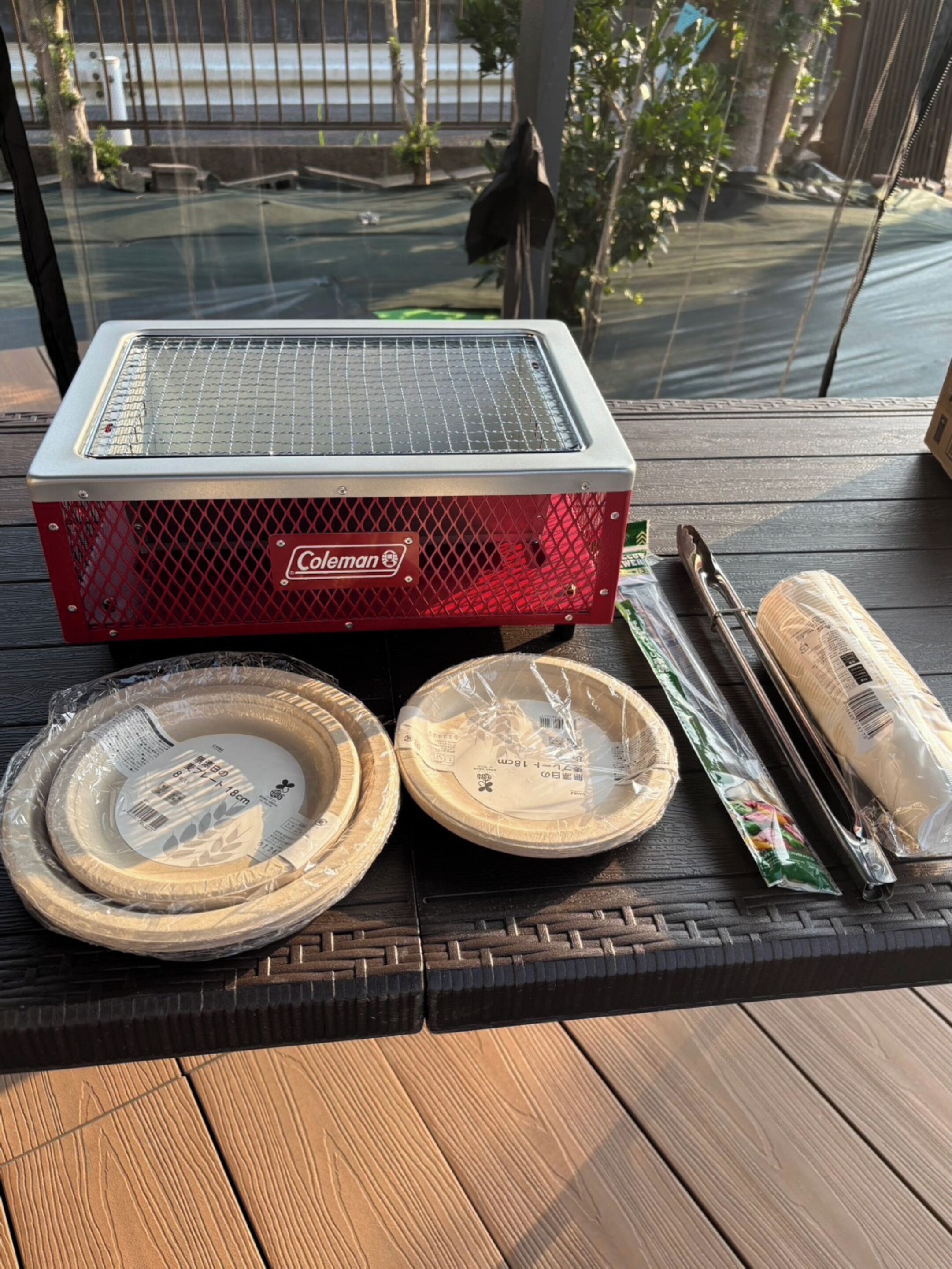 A Coleman portable grill on a wooden deck with two pizza boxes and a package of charcoal nearby.