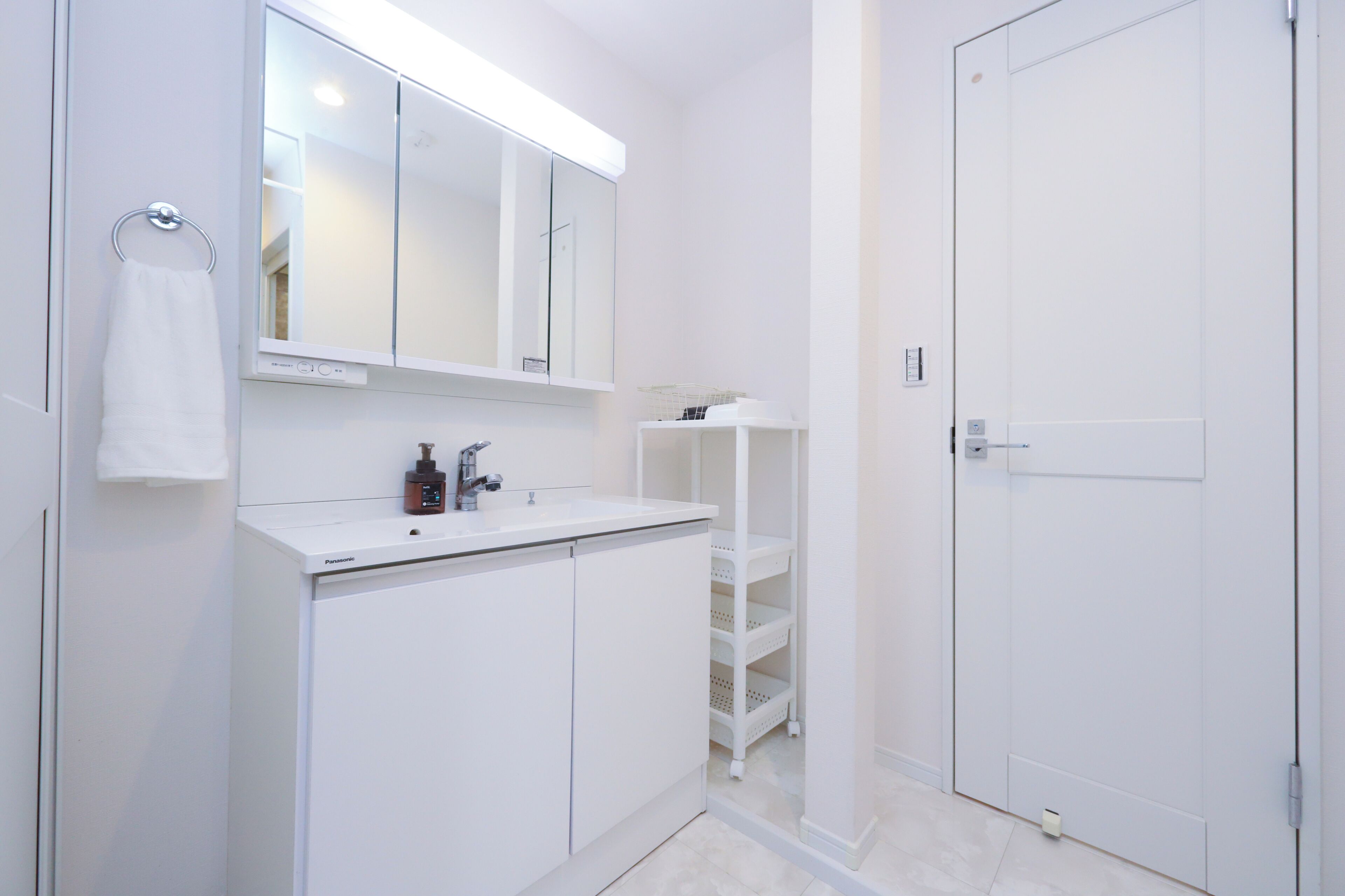 A modern bathroom with a white vanity, a mirror, a towel rack, and a door.