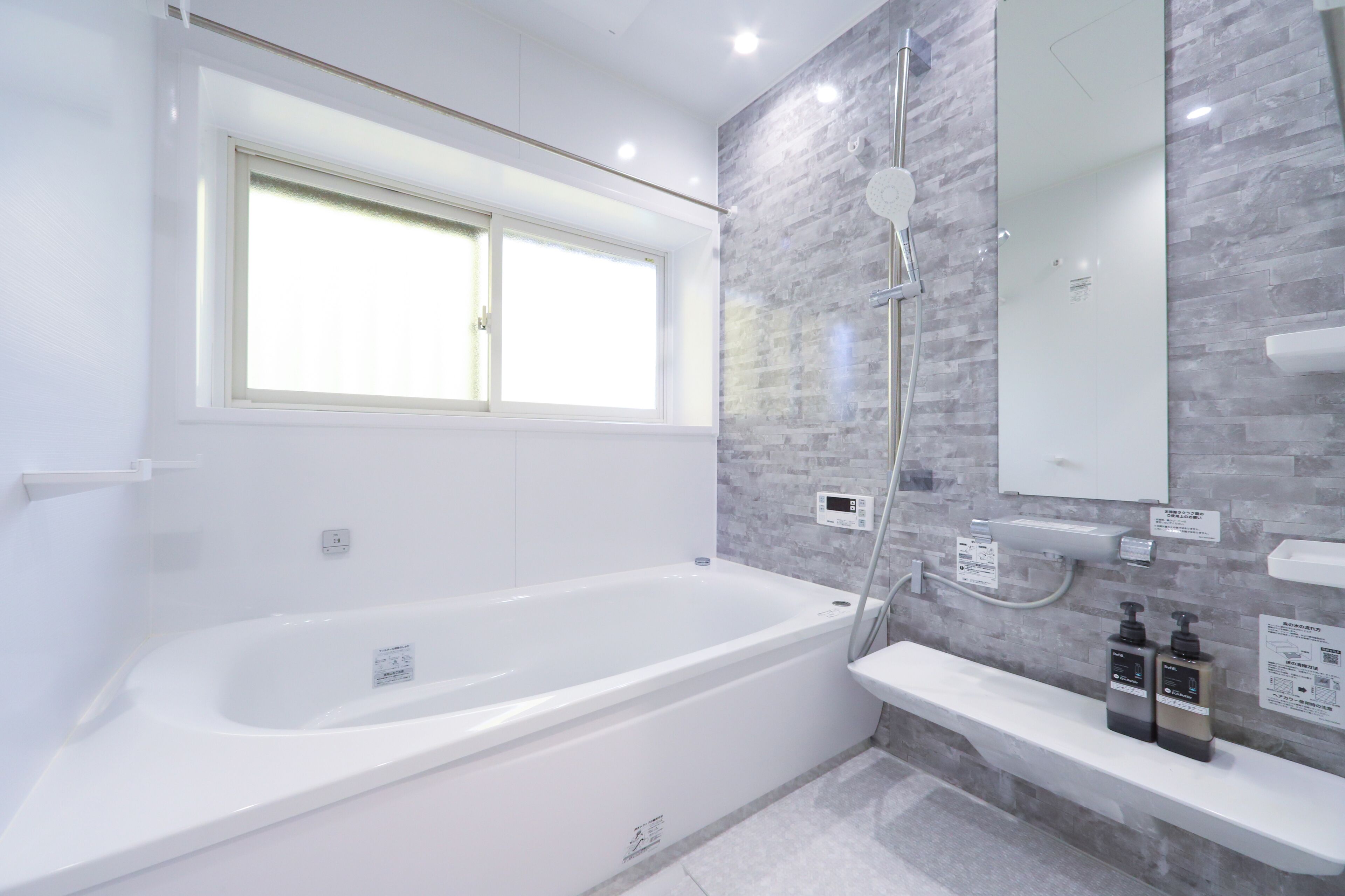 A modern bathroom with a white bathtub, a window, a shower, and a mirror.