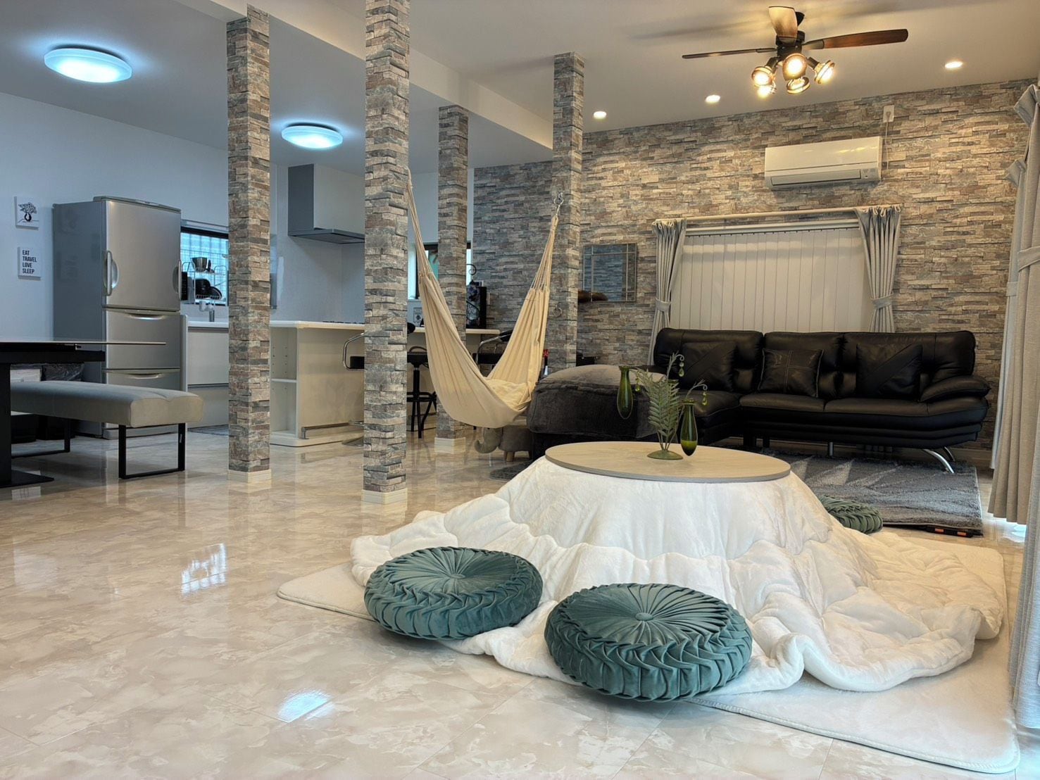 A modern living room with a stone wall, a black leather sofa, a white coffee table, and a hammock.