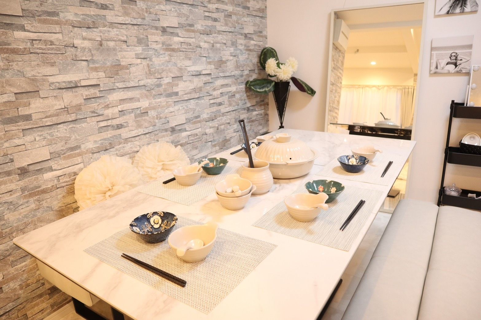 A dining table set with various bowls and chopsticks, a vase with flowers, and a stone wall in the background.
