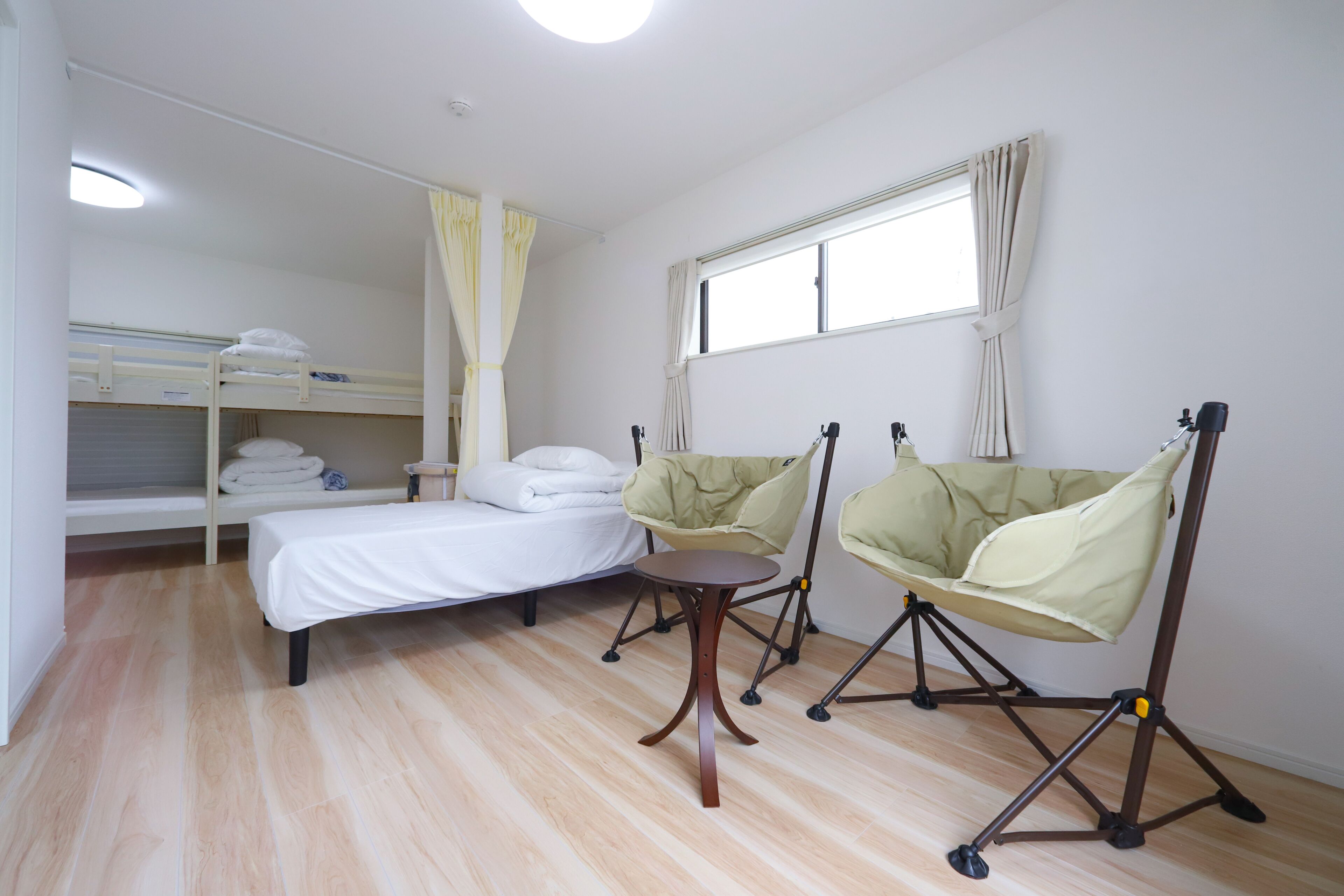 A room with a bunk bed, a single bed, a small table, two chairs, and a window with curtains.