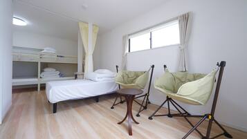 A room with a bunk bed, a single bed, a small table, two chairs, and a window with curtains.