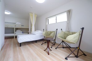 Una habitación con una litera, una cama individual, una mesita pequeña, dos sillas y una ventana con cortinas.